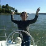 Windward Design Group Tina Marker celebrating on a sailboat with water and trees in the background.