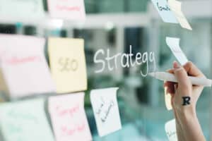 Business professional organizing marketing strategy with sticky notes on glass board.