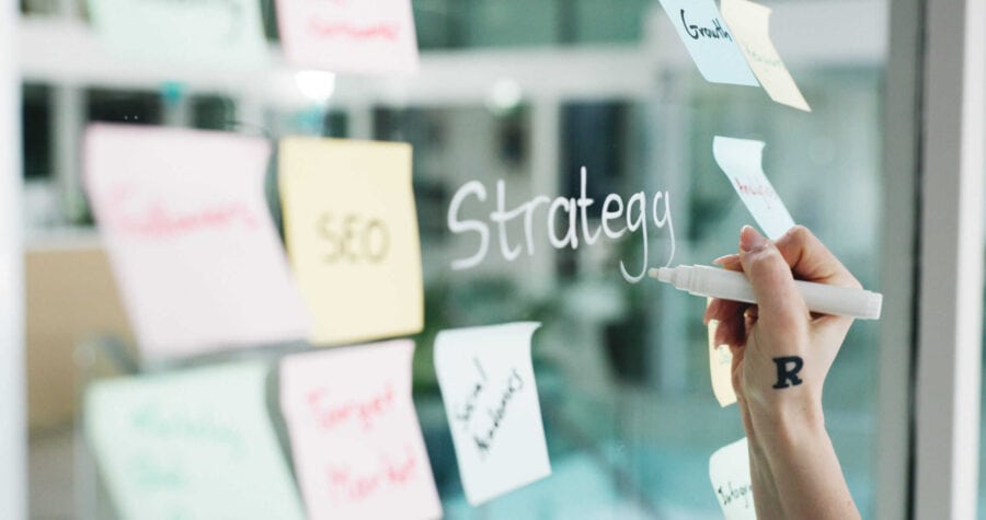 Business professional organizing marketing strategy with sticky notes on glass board.